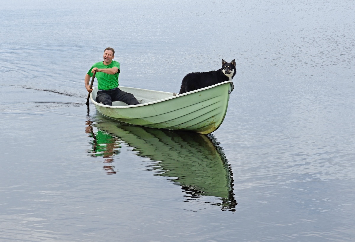 Man with dog on boat on lake. Taivalkoski, Finnish Lapland