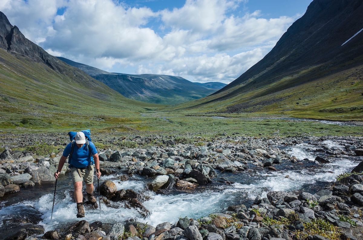Hiking in Swedish Lapland. Man trekking alone crossing river in northern Sweden. Arctic nature of Scandinavia in summer day